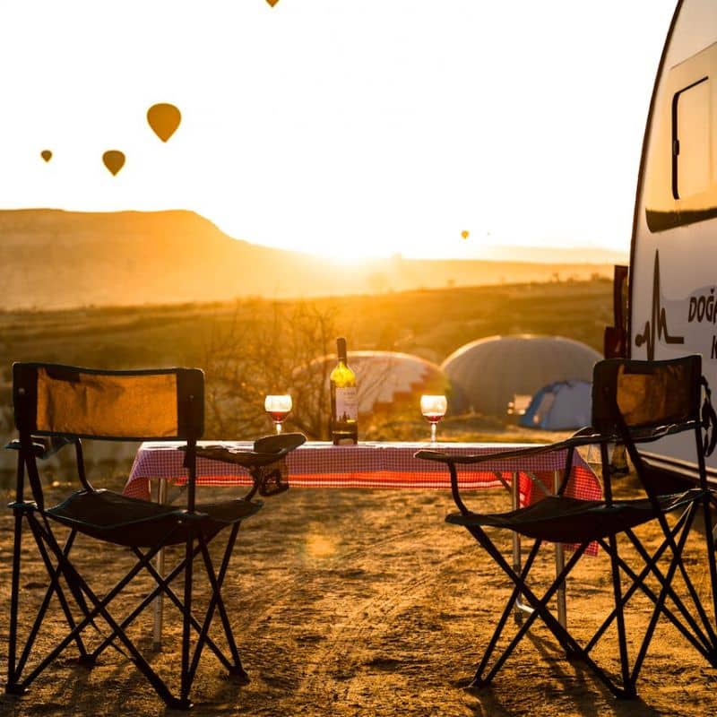 Une table et des chaises pliables de camping-car qui ont vue sur des montgolfières.